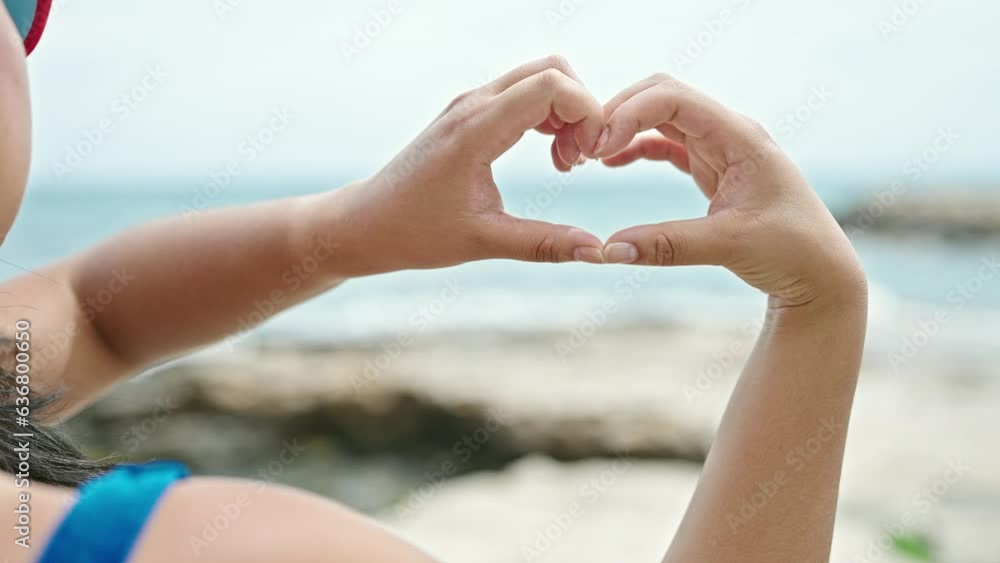 Young chinese woman tourist wearing bikini doing heart gesture at seaside Young chinese woman tourist wearing bikini doing heart gesture at seaside