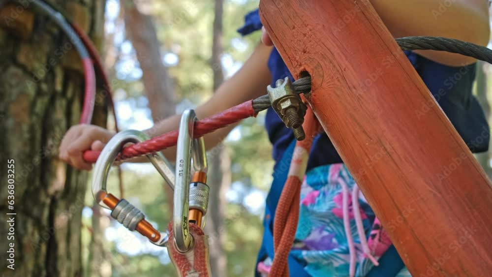 Caucasian Child Girl Attaching Double Spring Loaded Carabiner Snap Hook to Metal Safety Cable Line in Rope Park Obstacle Course Caucasian Child Girl Attaching Double Spring Loaded Carabiner Snap Hook to Metal Safety Cable Line in Rope Park Obstacle Course