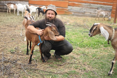 A farmer with a black curly beard with his Anglo Nubian goats © Владимир Коврижник