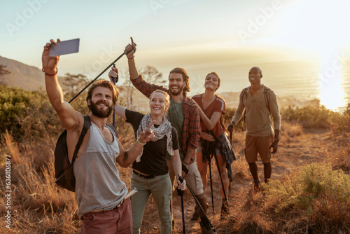 Diverse group of young people hiking and taking a moment to take a selfie with a smart phone overlooking a beautiful sunset and ocean