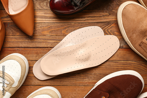 Pair of leather orthopedic insoles and different shoes on wooden background, closeup photo