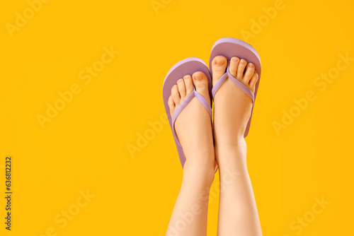 Female legs in stylish flip flops on yellow background