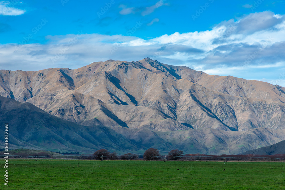 Fototapeta premium Photograph of a mountain range running behind a large green agricultural field with low level grey clouds on the South Island of New Zealand