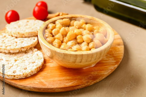 Bowl of fresh chickpeas covered with plastic food wrap and rice crackers on brown background