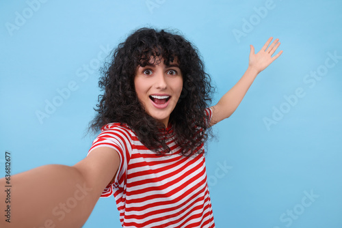 Beautiful young woman taking selfie on light blue background