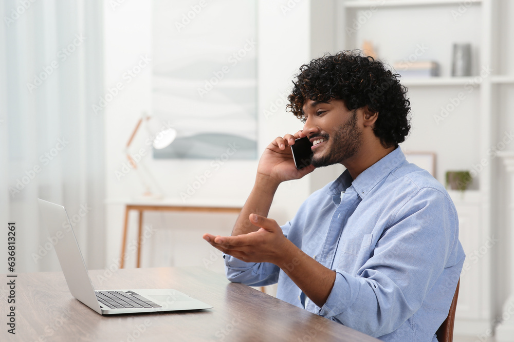 Handsome smiling man talking on smartphone in room, space for text