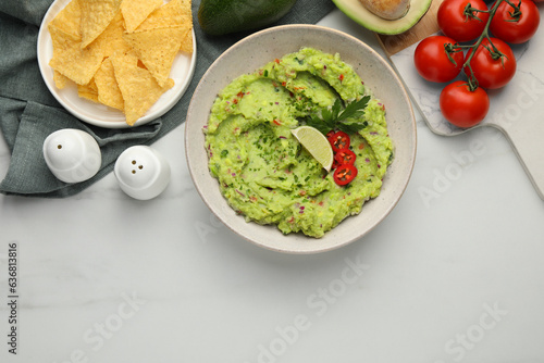 Delicious guacamole with nachos chips and ingredients on white marble table, flat lay. Space for text