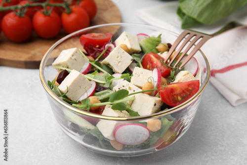 Bowl of tasty salad with tofu and vegetables on light grey table, closeup