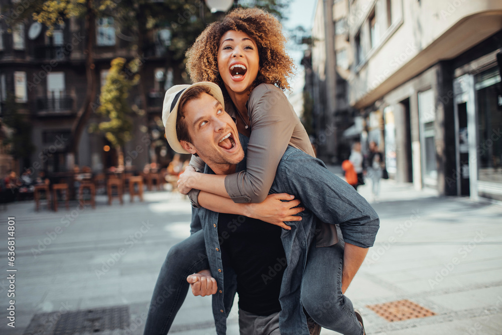 Young man carrying his girlfriend on his back while on a date in the city