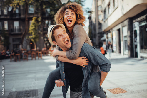 Young man carrying his girlfriend on his back while on a date in the city