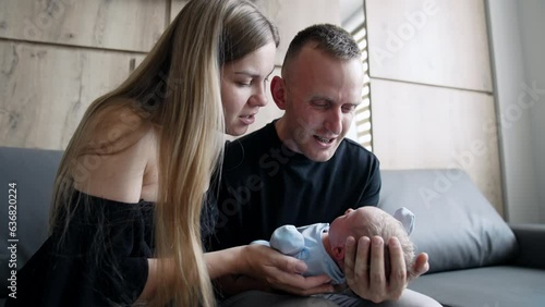 Caucasian new-made parents canoodling their newborn son. Parents sit on the sofa waving a baby and speaking to it.