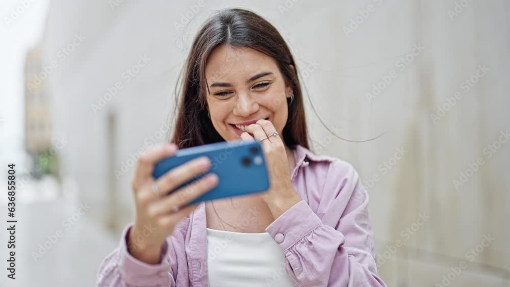 Young beautiful hispanic woman smiling confident watching video on smartphone celebrating at street Young beautiful hispanic woman smiling confident watching video on smartphone celebrating at street