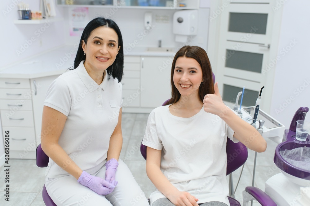 Obraz premium people, medicine, stomatology and health care concept - happy female dentist with patient girl talking at dental clinic office