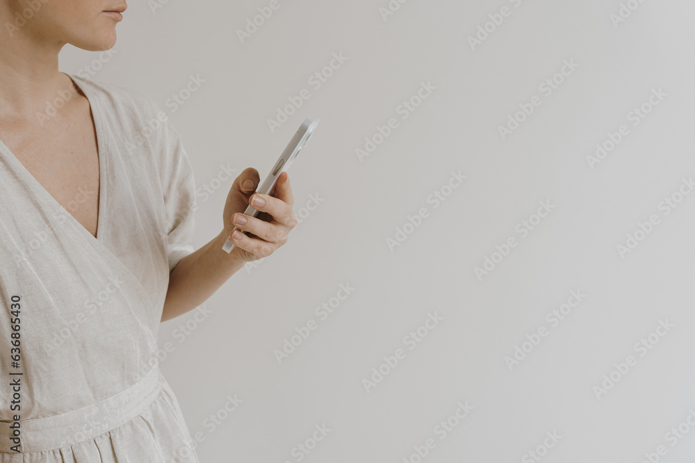 Mobile phone in female hands. Young pretty woman in neutral tan sandy beige linen dress Mobile phone in female hands. Young pretty woman in neutral tan sandy beige linen dress