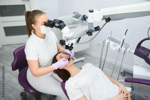 Female dentist using dental microscope treating patient teeth at dental clinic office