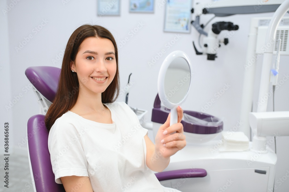Pretty girl in dentist cabinet is using a mirror to look through the ideal work of a doctor. Pretty girl in dentist cabinet is using a mirror to look through the ideal work of a doctor.