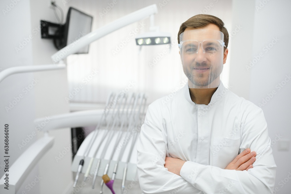 Attractive male dentist in doctors white lab coat posing in modern dental office Attractive male dentist in doctors white lab coat posing in modern dental office