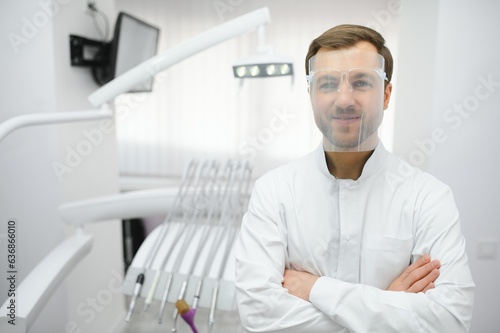 Attractive male dentist in doctors white lab coat posing in modern dental office