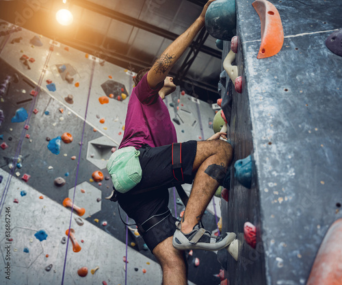 A strong male climber climbs an artificial wall with colorful grips and ropes. © romaset