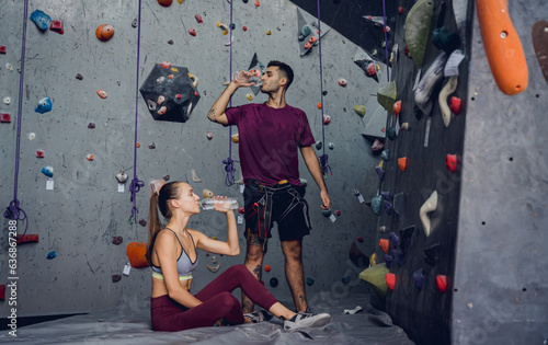 A strong couple of climbers relax near artificial wall with colorful grips and ropes.