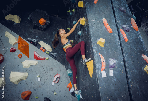 A strong female climber climbs an artificial wall with colorful grips and ropes.
