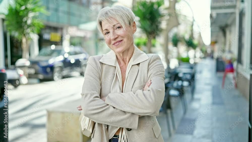 Middle age blonde woman smiling confident standing with arms crossed gesture at coffee shop terrace Middle age blonde woman smiling confident standing with arms crossed gesture at coffee shop terrace
