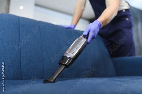 Professional janitor vacuuming armchair in room, closeup