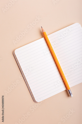 Opened white notepad with lined paper and pencil from above on beige background. Place for text.