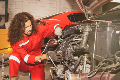 Professional male mechanic in a garage sits and examines the alternators, compressors, air conditioners and systems in cars that need to be replaced and reinstalled after a car crash and accident.