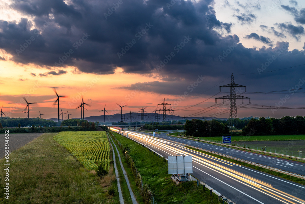 Langzeitbelichtung der Autobahn, Lichtspuren, Sonnenuntergang, Windräder und Strommasten