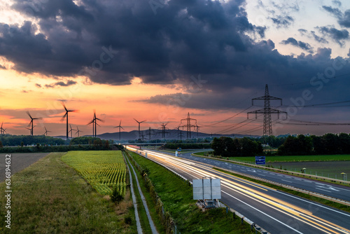 Langzeitbelichtung der Autobahn, Lichtspuren, Sonnenuntergang, Windräder und Strommasten