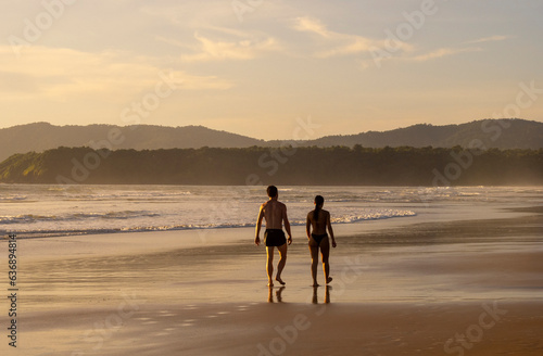 Young couple walking along seashore during summer sunset