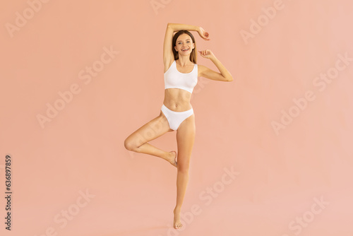 Full length shot of slim lady posing in underwear with hands behind her head, showing perfect body shape over nude pink studio background, copy space