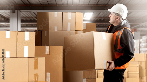 Man warehouse employee. Guy with cardboard boxes. Factory warehouse worker. Storekeeper in reflective vest. Loader picks up box. Parcel warehouse inside hangar. Man storekeeper at work