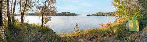 panorama of the river bank and the forest with the morning sun through the trees, the green tent of the resting people