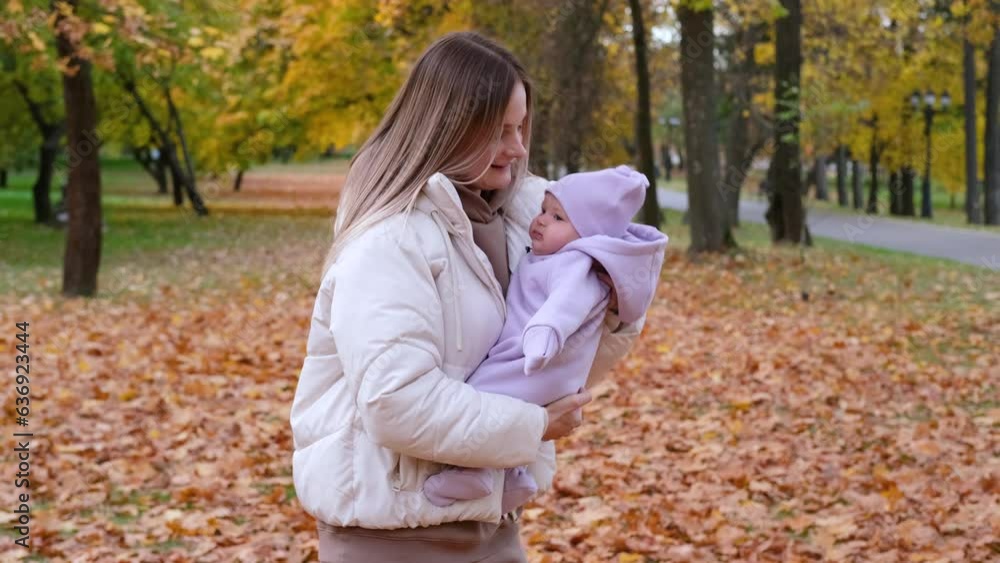 Young mother with newborn baby in autumn park. Mother shakes the child in her arms so that the girl does not cry. Slow motion horizontal video Young mother with newborn baby in autumn park. Mother shakes the child in her arms so that the girl does not cry. Slow motion horizontal video