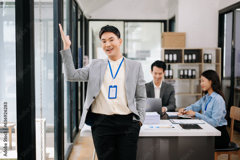 Young attractive Asian male office worker business suits smiling at camera with working notepad, tablet and laptop documents in office Young attractive Asian male office worker business suits smiling at camera with working notepad, tablet and laptop documents in office