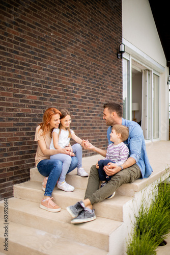 Family with a mother, father, son and daughter sitting outside on the steps of a front porch of a brick house