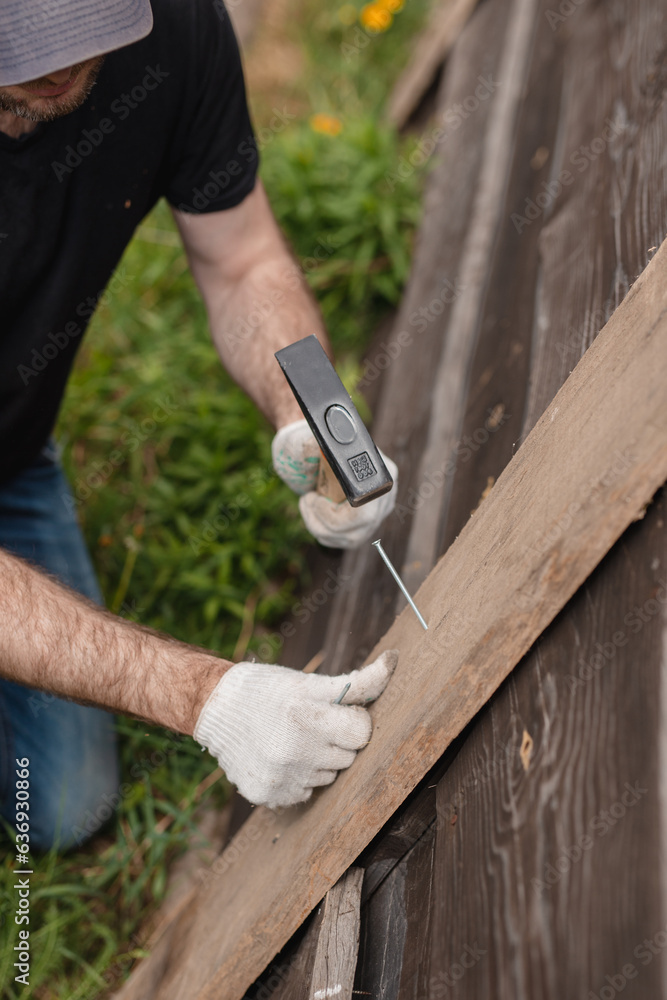A man builds and paints a fence from rough boards - rustic processing style - summer warm day