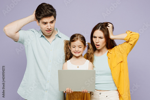 Young scared IT parents mom dad with child kid daughter girl 6 years old wearing blue yellow casual clothes hold use work on laptop pc computer isolated on plain purple background. Family day concept. photo