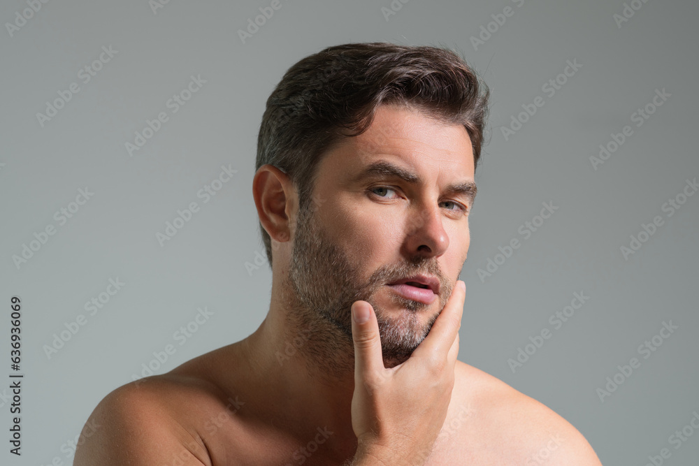 Obraz premium Close-up portrait of perfect brunet man touching chin and skin. Handsome man touching face in gray studio isolated background. Perfect skin. Man cosmetic, skin treatment. Hygiene skin care male face.
