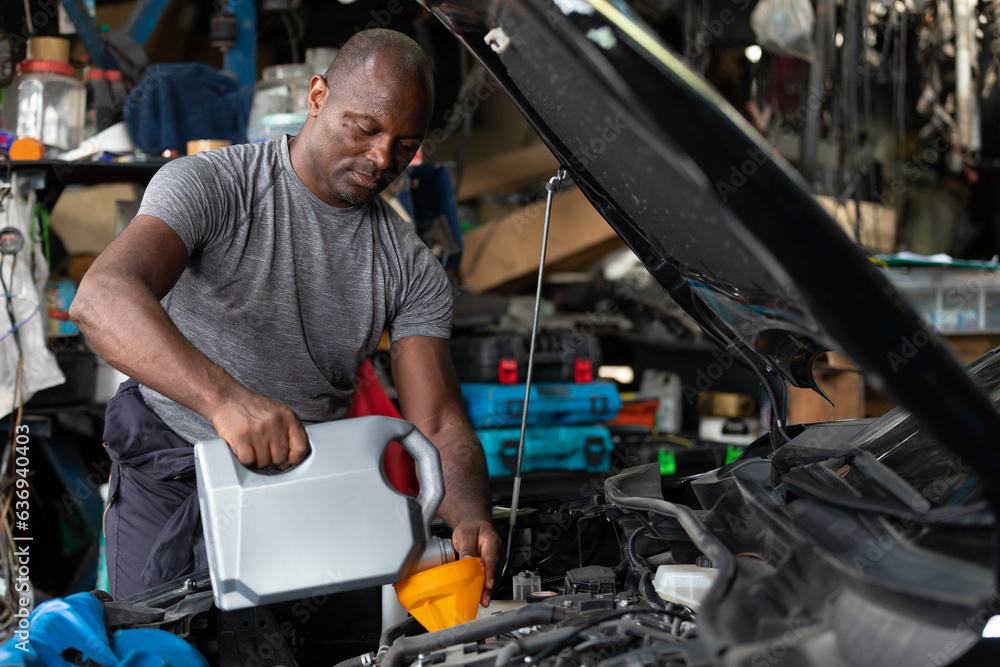 African mechanic worker filling engine oil into a car in garage African mechanic worker filling engine oil into a car in garage