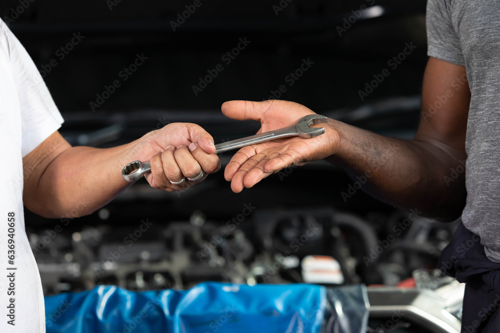 closeup mechanic hands giving wrench to coworker for fixing a car in automobile repair shop