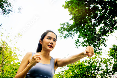 Vászonkép Recreation young asian woman exercising in the park : Beautiful asian woman warming up practicing boxing using her fists to exert force punching the air alternately left and right attentively