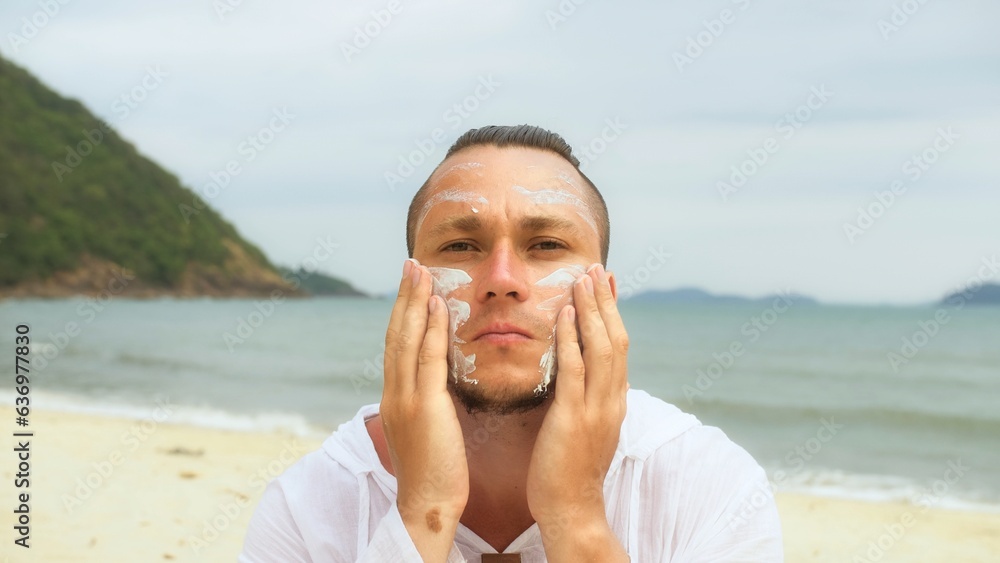Portrait man apply sun cream protection lotion.Man looking at camera, relax on beach near sea smearing sunscreen cream on face.Concept facial beauty skin care, moisturizer cosmetic, hygiene treatment Portrait man apply sun cream protection lotion.Man looking at camera, relax on beach near sea smearing sunscreen cream on face.Concept facial beauty skin care, moisturizer cosmetic, hygiene treatment