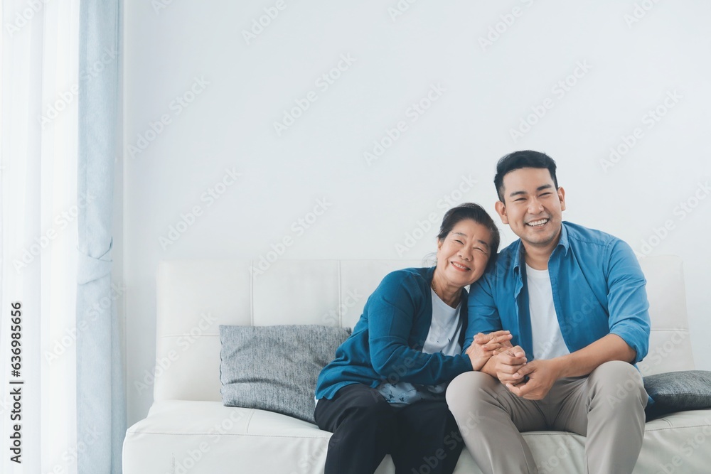 Happy Asian senior with smiling Asian man sitting sofa in living room ,Portrait Happy mother and son in living room ,Happiness family concept. Happy Asian senior with smiling Asian man sitting sofa in living room ,Portrait Happy mother and son in living room ,Happiness family concept.