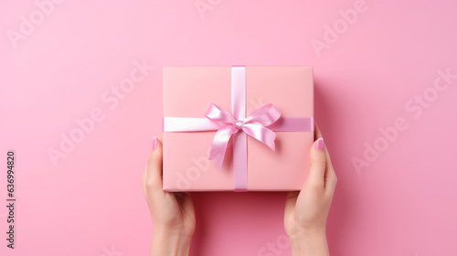 Hands of a girl with a manicure holding a gift box with a bow on a pink background