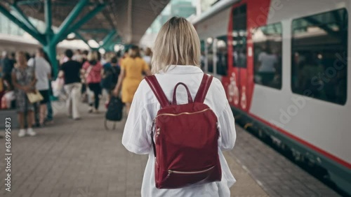 A woman at the train station walks on a platform next to commuter trains. Daily use of public transport in urban life.