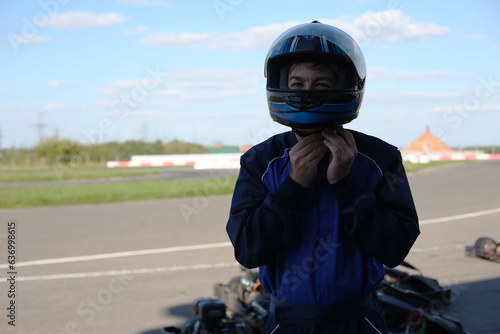 Male race car driver trying to fasten the clasp on his helmet before a race
