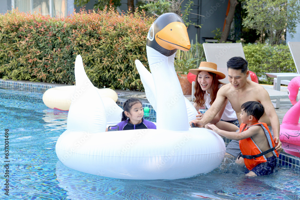 Naklejka premium Happy Asian family, father mother daughter and son enjoy outdoor activity at pool, kid and parent swimming with white swan plastic toy in blue water, relaxing family has fun together on summer holiday